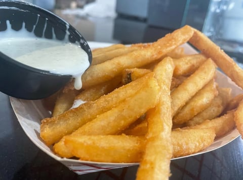 Golden fried potato fries in paper wrapper with a small bowl of white dipping sauce