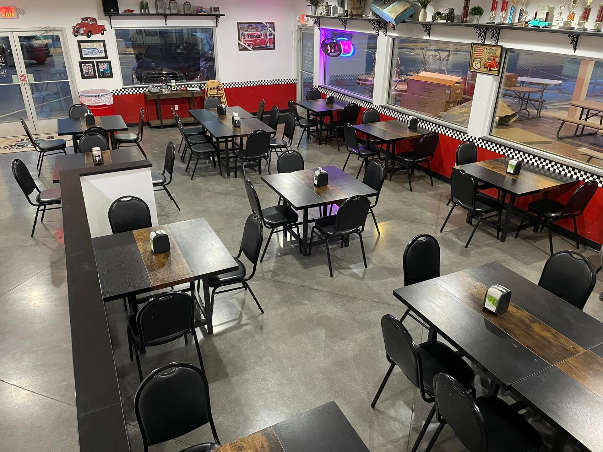 Retro diner interior with red booth seating, black dining tables, chairs, neon signs, and vintage decor