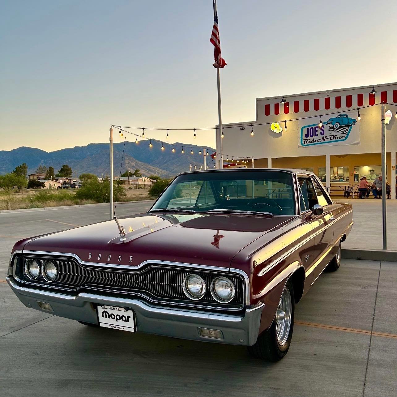 Classic burgundy and gold Dodge Mopar from the 1960s parked outside a vintage diner with mountains in the background