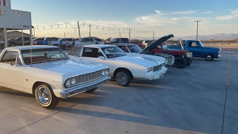 Row of classic cars displayed at outdoor car show, including light blue vintage sedans and trucks with open hoods
